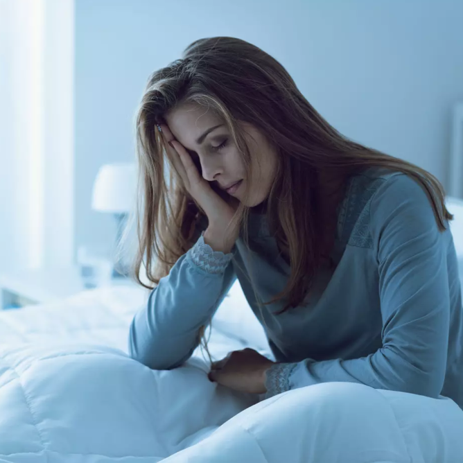Femme fatiguée souffrant d'insomnie, assise sur un lit la nuit, illustrant le lien entre le manque de sommeil et les spasmes des paupières